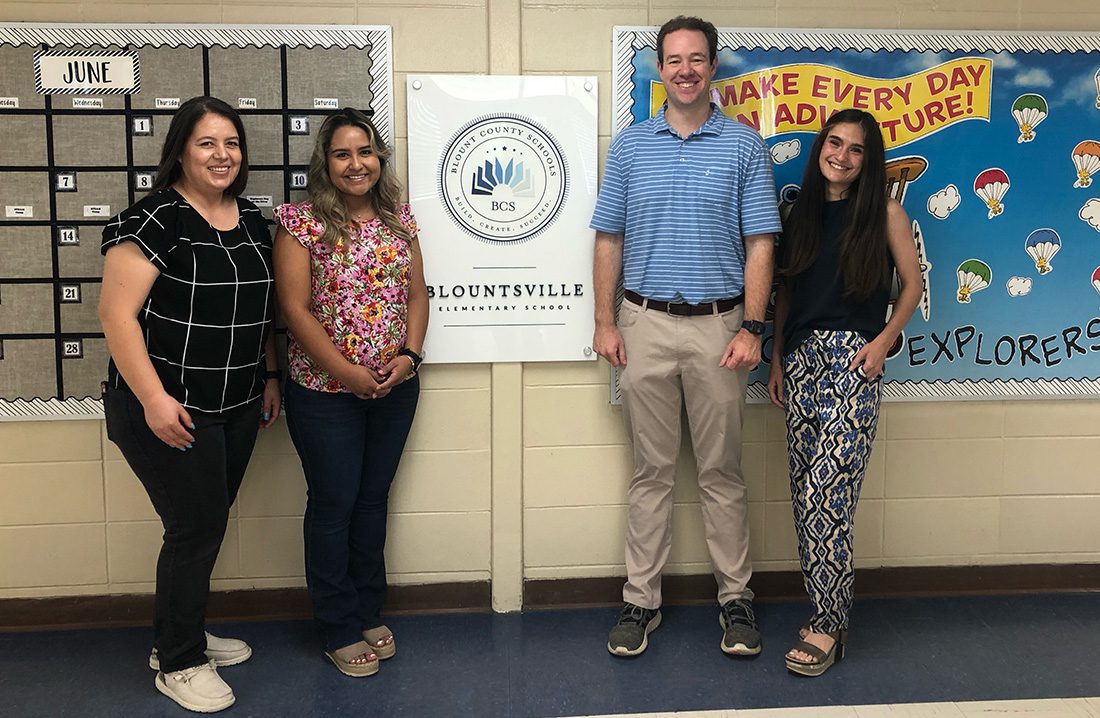 Referral Program - Allison Insurance Team Smiling and Standing Together for a Photo in Front of a Wall with Announcements and a June Calendar Board